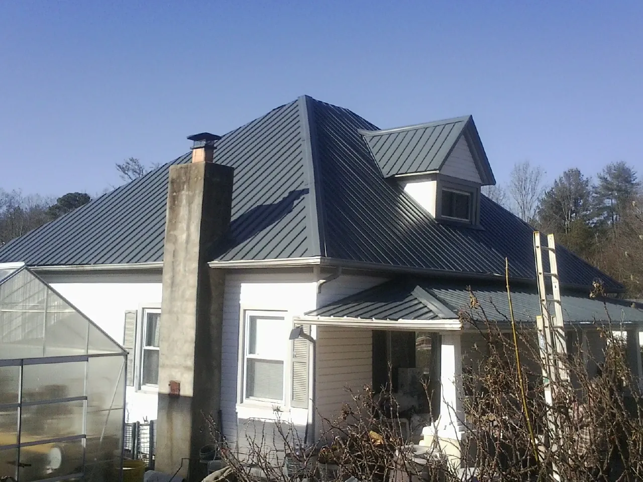 Dark blue standing seam metal roof on a white farmhouse with dormer — Slate & Tile Roof Repair by Roofing Brothers in Dodgeville