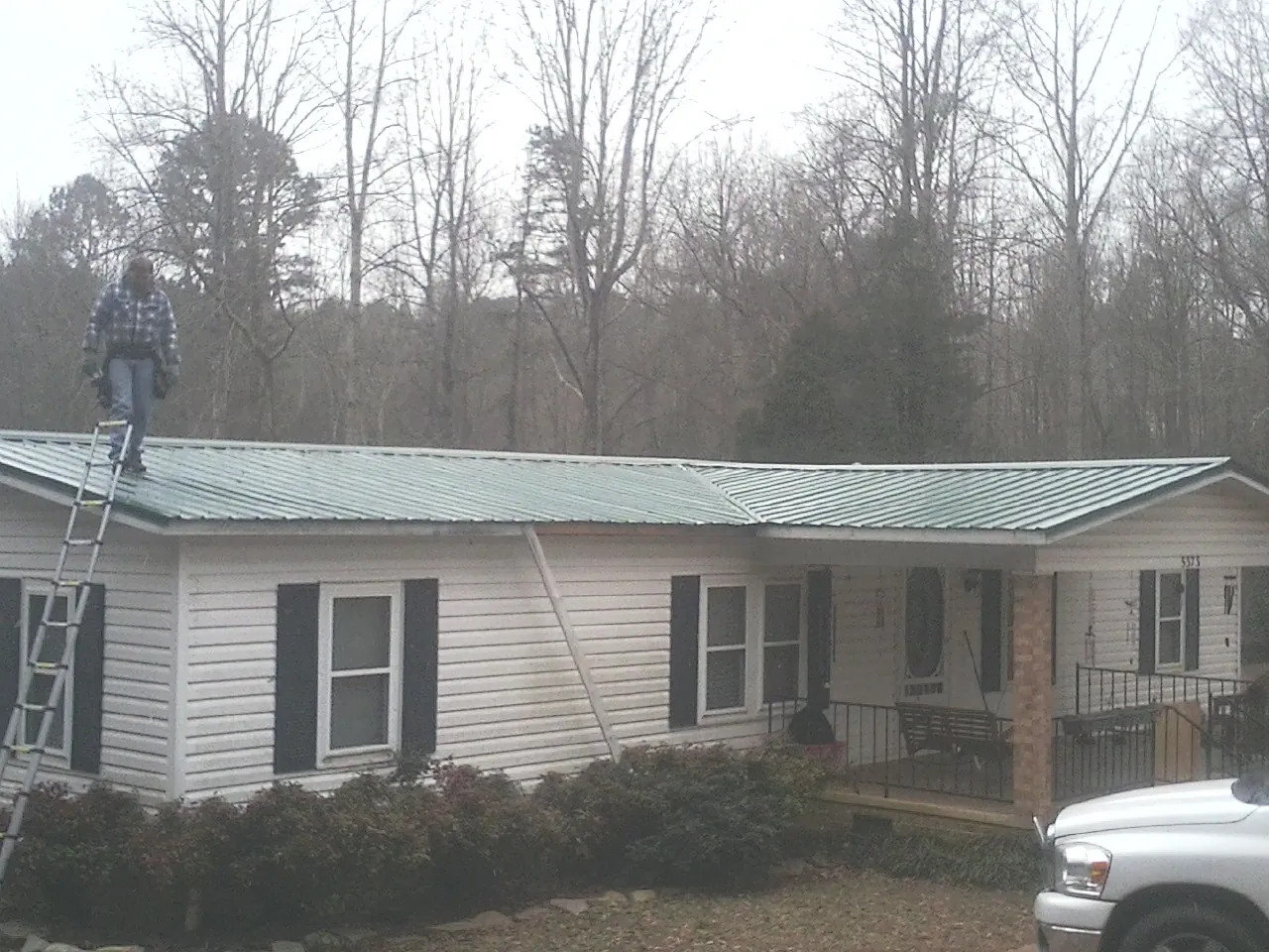 Worker on a ladder beside a new green metal roof on a ranch home in Dodgeville