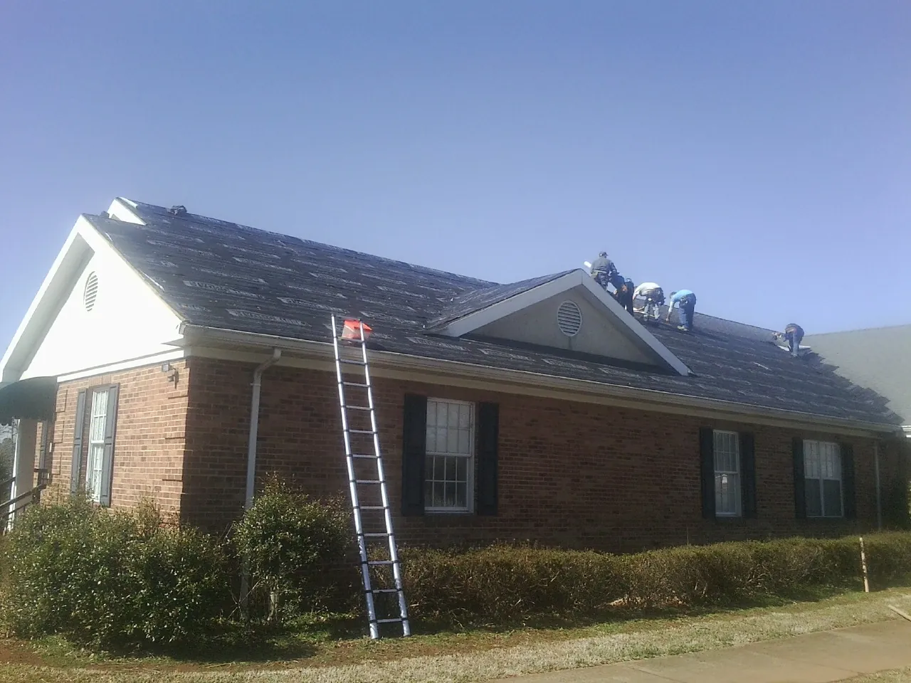Crew tearing shingles off a brick ranch roof with a ladder set — Metal Roof Repair work by our crew in Dodgeville