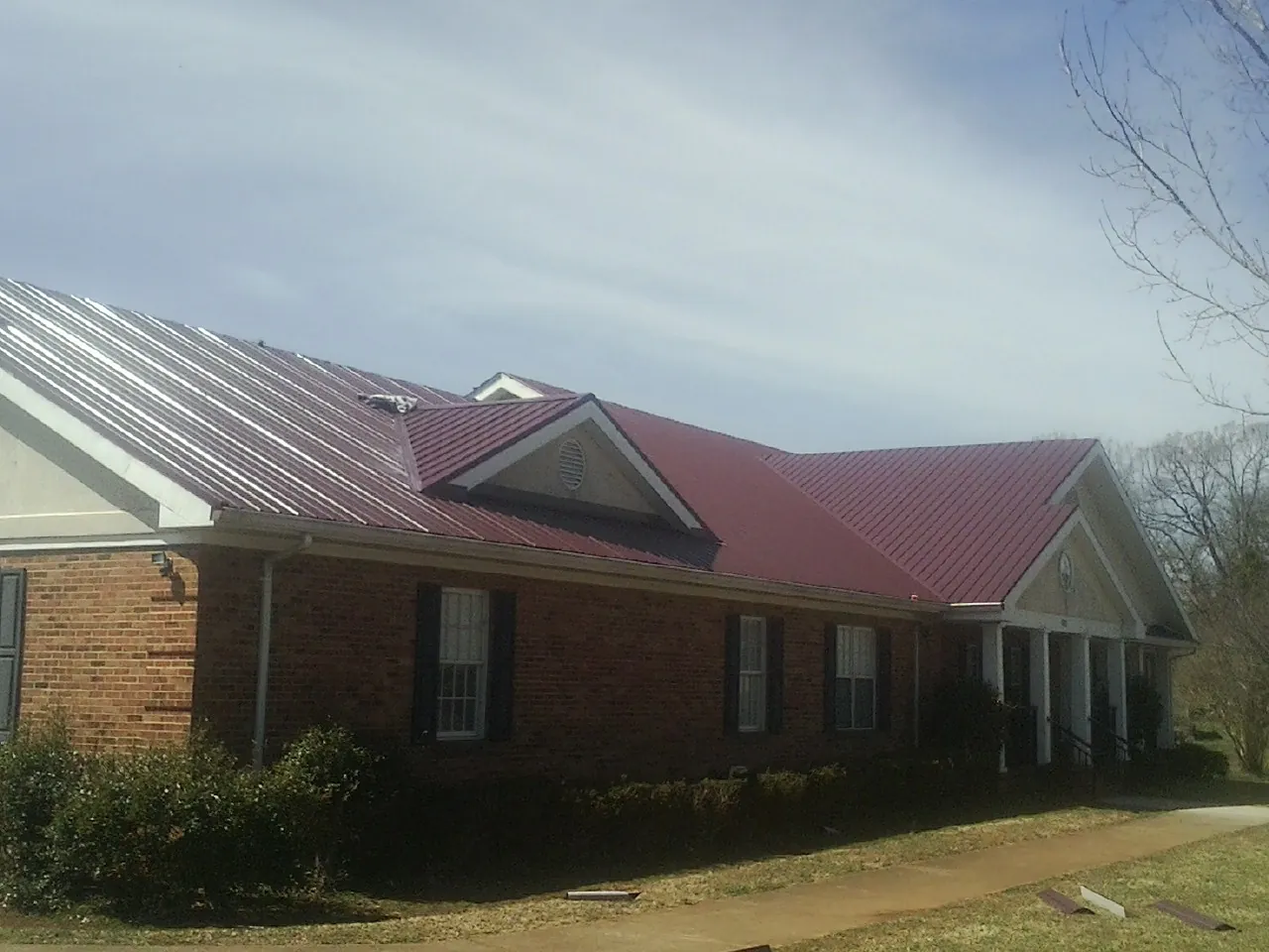 Red metal roof with gabled entries on a long brick building, from a Hail Damage Roof Repair job in Dodgeville