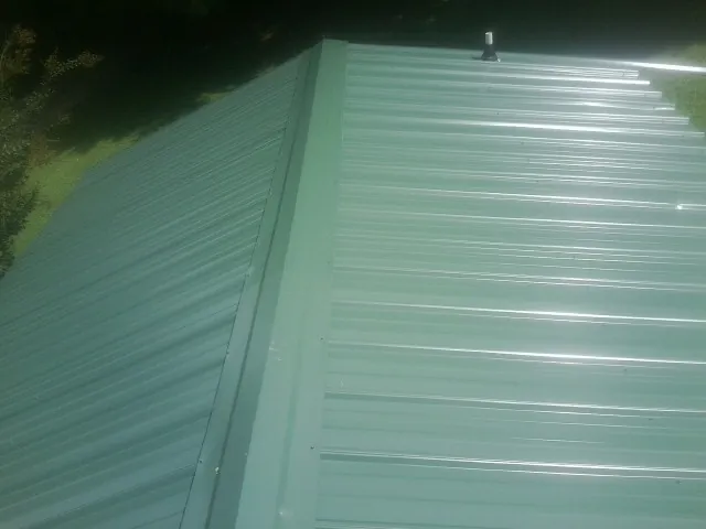 New green metal panels meeting at the ridge of a roof — Flat Roof Repair work by our crew in Dodgeville
