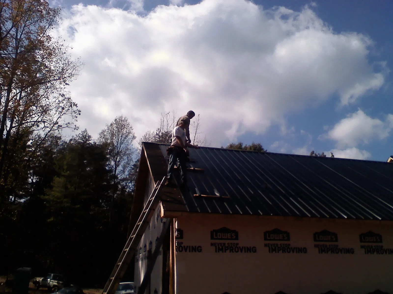 Roofer fastening dark metal panels high against a cloudy sky, from a Roof Inspection job in Dodgeville