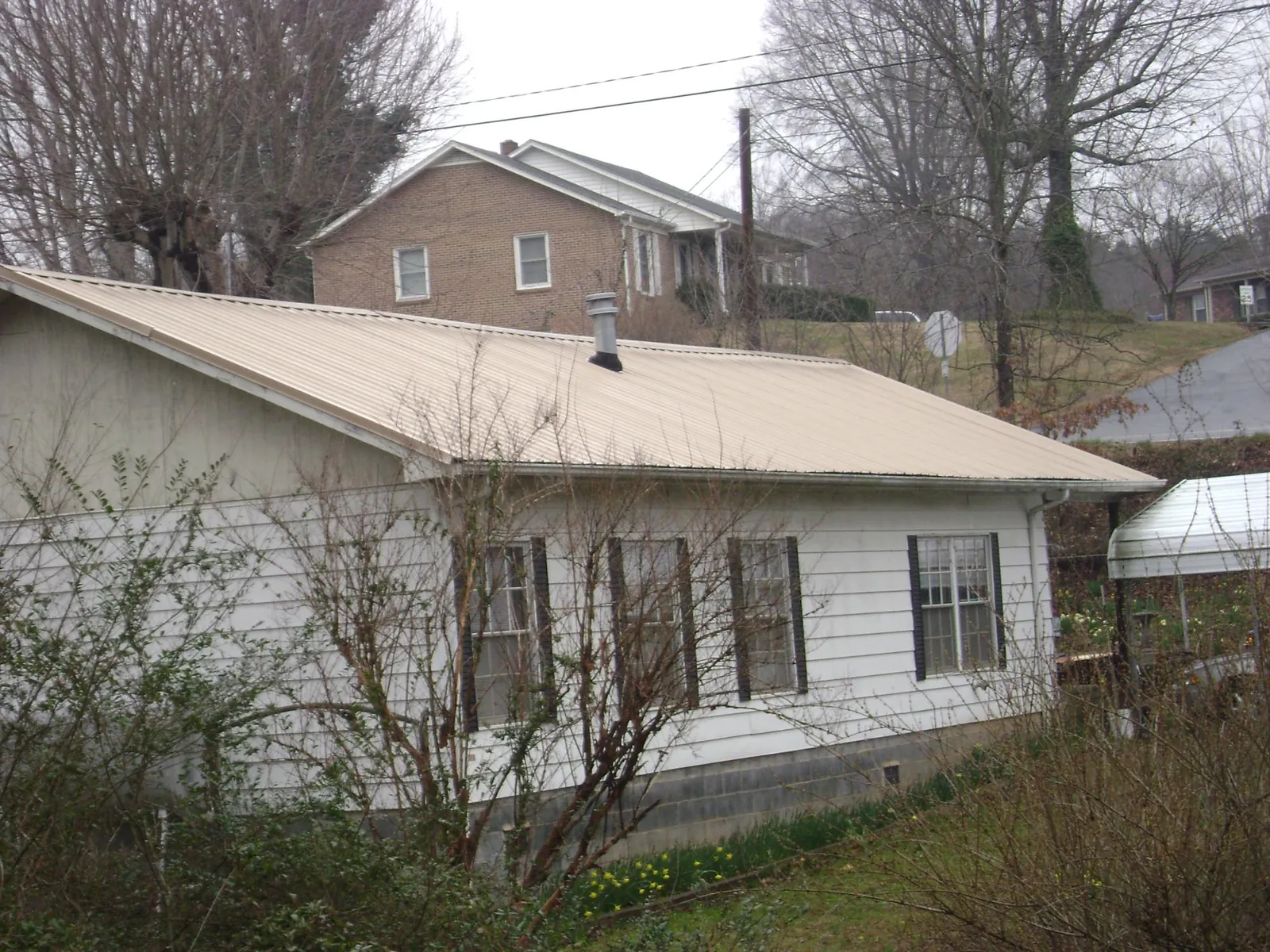 Tan metal roof on a white sided house set into a hillside — Commercial Roofing by Roofing Brothers in Dodgeville